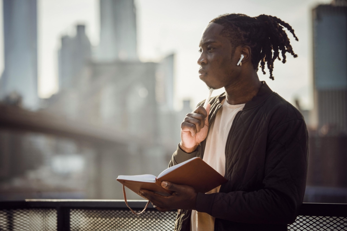 Thoughtful man in wireless earphones with notepad on a balcony.