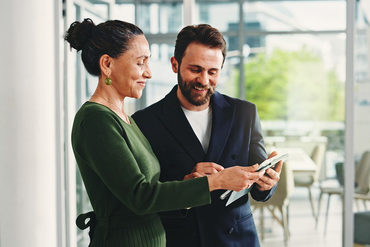 A male and female colleague looking at a tablet together in a bright office.