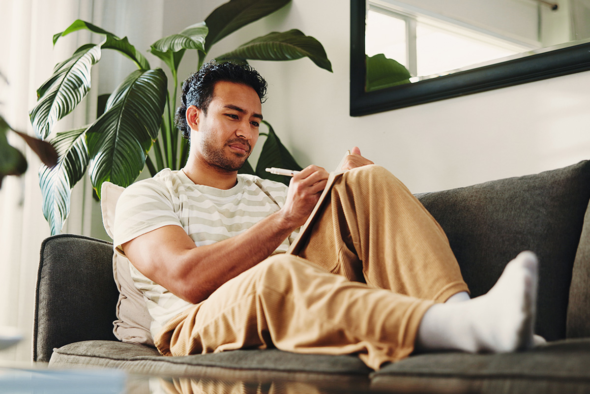 A man sitting on his couch while writing notes in a journal.